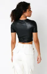 Crop top negro de cuero sintético, elastizado y forrado, con busto marcado estilo corset y mangas cortas.