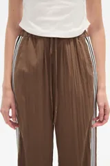 Pantalón de algodón negro, holgado, de calce medio, con cintura elástica y cordón ajustable. Presenta tres rayas blancas verticales en los laterales.