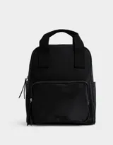 Mochila negra de cuerina con doble asa corta de mano con textura, correas regulables, cierre superior, bolsillo frontal con cierre, bolsillos laterales y tag en relieve.
