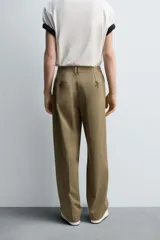 Pantalón color caqui de corte tapered relaxed fit, confeccionado en tejido de algodón. Presenta cintura con pliegues frontales dobles, bolsillos laterales en cadera y bolsillos traseros de vivo con botón. Cierre frontal con cremallera y botón.