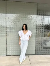 Blusa blanca con escote en V, mangas cortas con volados y lazos en el escote.