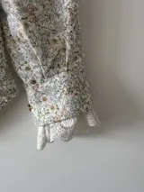 Camisa blanca estampada con flores pequeñas en tonos celeste, rosa y amarillo. Confeccionada en lino 100%, con botones de nácar y puntilla de algodón en los puños.