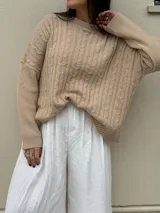 Sweater color beige con cuello redondo y diseño de trenzas en relieve.