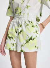 Short de tela con estampado floral en tonos blanco, verde y amarillo. Cintura elástica con cordón ajustable y puntas metálicas, bolsillos laterales y traseros.