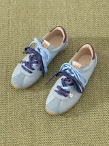 Zapatilla de cuero marrón con detalles en verde y suela de goma. Tiene cordones rosas y un dije colgante con forma de abeja.