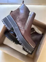 Botines negros de cuero con caña baja, puntera redondeada y cierre frontal con cremallera. Presentan paneles laterales de gamuza y suela track con plataforma.