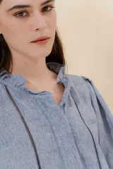 Blusa color beige con cuello mao con volantes, manga larga con puño elástico y cierre frontal con botones ocultos.