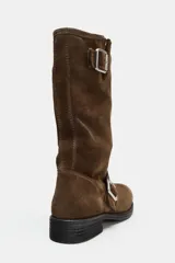 Botín plano de estilo motero en serraje color marrón, con punta redonda. Presenta dos tiras con hebillas metálicas, una en la caña y otra en el empeine. La suela tiene una altura de 4 cm.