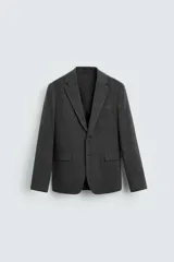Blazer gris oscuro de corte regular fit confeccionado en tejido con 17% de lana. Tiene cuello con solapas de muesca, manga larga con puño abotonado, bolsillo de vivo en el pecho, bolsillos de solapa en la cadera, bolsillo interior, aberturas en la espalda y cierre frontal con botones.