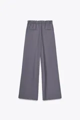 Pantalón gris de tejido fluido, tiro alto con cintura tipo paper bag, bolsillos laterales y cinturón lazada en el mismo tejido.