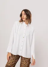 Camisa blanca de cuello redondo con frunces, abotonada y de manga larga con puño abierto.