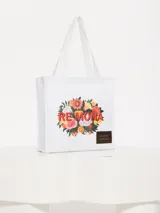Bolso tipo tote de algodón blanco con estampado de flores y texto "RE MONA" en rojo. Tiene asas de mano y un parche de cuero sintético con texto grabado.