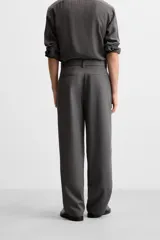Pantalón negro de corte ancho con cinturón de tela con hebilla metálica y pliegues frontales.