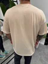 Remera color beige de punto símil tejido, corte holgado y mangas cortas.