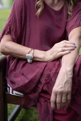 Brazalete abierto de metal dorado con dos piedras ovaladas centrales, una superior rodeada de pequeñas piedras brillantes y una inferior lisa de tono rosado pálido.