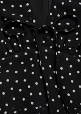 Vestido corto negro con estampado de lunares blancos, escote en V con lazo, mangas cortas y falda con volantes.