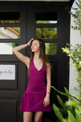 Vestido corto color fucsia, con escote en V y breteles finos que se atan atrás del cuello. Tiene corte en la cadera y falda con ruedo irregular y pico en lateral.