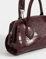 Bandolera color borgoña de cuerina con efecto croco, doble asa corta de mano, correa regulable y desmontable, doble cierre superior y puller de material principal.