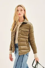 Campera puffer color beige con cuello camisero, cierre con botones a presión, bolsillos con solapa en el pecho y relleno de plumas.
