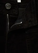 Pantalón culotte de pana negra, tiro alto, con cierre de cremallera y botón, trabillas, dos bolsillos de parche delanteros y dos traseros. Diseño crop.