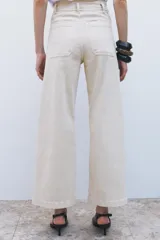 Pantalón de jean de tiro alto color negro con pierna ancha, bolsillos delanteros y traseros, y cierre frontal con cremallera y botón metálico.