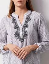 Blusa de gasa bambula a rayas verticales celestes y blancas, con cuello a la base, escote en v con botones y bordado negro. Mangas largas regulables con presilla y botón.