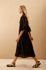 Vestido largo negro con estampado de lunares dorados, mangas al codo y corte amplio con ajuste elástico en la cintura. Presenta bordados de lentejuelas y mostacillas en el escote y mangas.