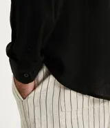 Camisa negra de lino con corte clásico, cuello camisero y mangas largas. Cierre frontal con botones.