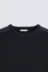 Jersey negro de punto con cuello redondo y manga larga. Presenta parches combinados en hombros y codos.