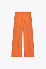 Pantalón ancho color naranja, de tiro medio y cintura con trabillas. Tiene bolsillos laterales y de vivo en espalda, pinzas en delantero, raya planchada y cierre frontal con cremallera, botón y ganchos metálicos.