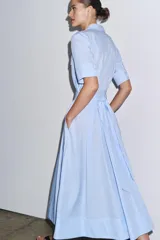 Vestido camisero midi de popelín a rayas verticales celestes y blancas, con cuello solapa, manga corta, bolsillos de plastrón con solapa en el pecho, cinturón de lazo ajustable y cierre frontal con botones.