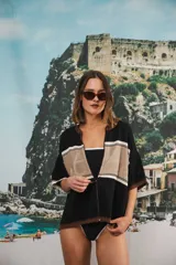 Remera de tejido calado color crudo con rayas horizontales rojas y terminaciones marrones, con cierre frontal y logo bordado.