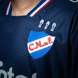 Camiseta de fútbol Umbro del Club Nacional de Football, modelo Away 2. Diseño azul marino con detalles en blanco y rojo en cuello y mangas. Incluye logo de Umbro, escudo del club y sponsor Antel en el frente.