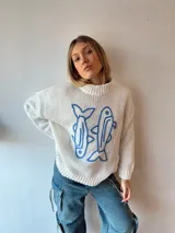 Sweater de punto color crema con cuello alto y estampado de dos peces azules en el frente.