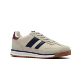 Championes deportivos de estilo retro, color dorado metalizado con efecto craquelado. Presentan tres franjas laterales negras y detalles en negro en el talón y ribetes. La suela es de goma color caramelo con entresuela blanca.