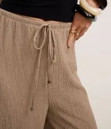 Pantalón wide leg color beige con textura, cintura elástica con cordón ajustable y bolsillos laterales.