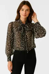 Blusa de poliéster estampada con motivo animal print en tonos grises y negros. Tiene cuello a la base con lazo para atar, mangas largas abullonadas y corte recto.