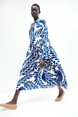 Vestido midi de viscosa con estampado floral azul sobre fondo blanco, cuello camisero, tapeta de botones oculta, mangas raglán largas con puños sencillos y costuras fruncidas en la falda.