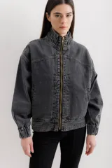 Campera tipo bomber de jean negro con cierre frontal dorado, bolsillos laterales y cuello alto. Tiene mangas largas con puños elastizados y detalles de costuras a contratono en cuello y pretina.