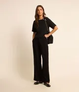 Blusa negra de crepé con cuello redondo, mangas cortas y botones decorativos dorados en los hombros.