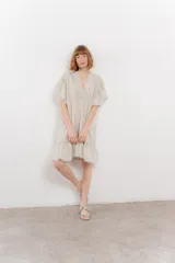 Vestido corto color beige confeccionado en algodón, con escote en V con detalles bordados, mangas cortas amplias con volados y falda con ruedo en volado.