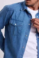 Camisa de jean celeste de manga larga con cuello clásico, cierre con botones a presión y dos bolsillos con solapa abotonada en el pecho.