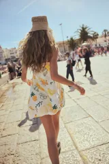 Vestido corto blanco con estampado de bananas, limones, piñas y sombrillas. Tiene breteles finos ajustables, escote corazón y cuerpo entallado con frunces en el escote y laterales. La falda es levemente acampanada.