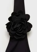 Traje de baño enterizo negro con escote halter y espalda descubierta. Presenta detalle de flor grande en el cuello.