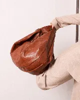 Bolso marrón oscuro de cuero sintético con forma ovalada y asa corta.