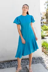 Vestido color naranja con escote redondo, largo asimétrico y espalda descubierta con cierre de botón. Tiene mangas cortas abullonadas con elástico.