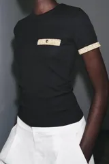 Camiseta blanca de corte slim fit, cuello redondo y manga corta. Detalle de acabados en tricot con hilo metalizado color dorado en mangas y bolsillo.