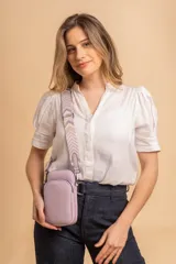 Bandolera pequeña tipo 'phone bag' de símil cuero color rosado pálido, con cierre de cremallera y correa ancha de tela con diseño de chevron en tonos claros.