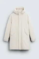 Parka color crudo de tejido técnico acolchado, con cuello alto y capucha ajustable. Tiene mangas largas con puños ajustables, bolsillos frontales con solapa, bolsillo interior y cierre frontal con cremallera oculta por solapa con botones a presión.