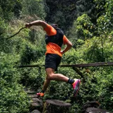Remera deportiva naranja de poliéster y spandex, con logo Merrell estampado en el pecho.